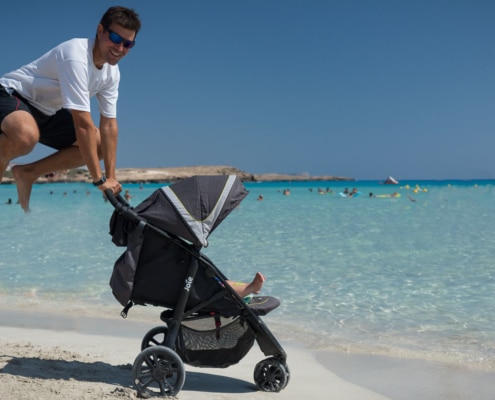 Zypern mit Kindern - Mann springt am Strand hoch am Kinderwagen
